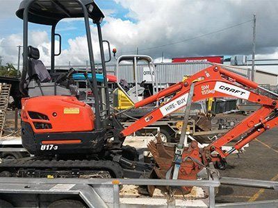 An orange Kubota U17-3 compact excavator is secured on a flatbed utility trailer in an outdoor storage yard.