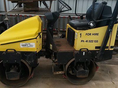 A yellow, dual-drum walk-behind roller for hire, parked on a concrete surface.