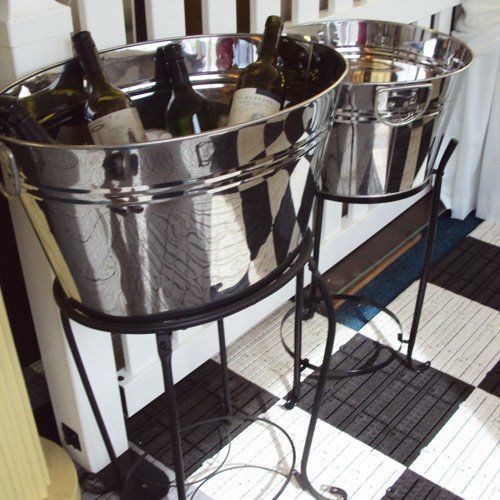 Two silver metal beverage tubs holding wine bottles on black wrought iron stands, set on a black and white tiled floor.