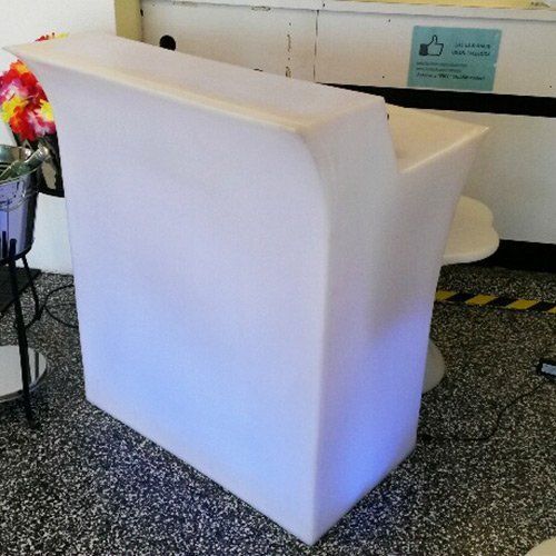A white, illuminated, semi-circular portable bar counter standing on a speckled floor in an indoor setting.