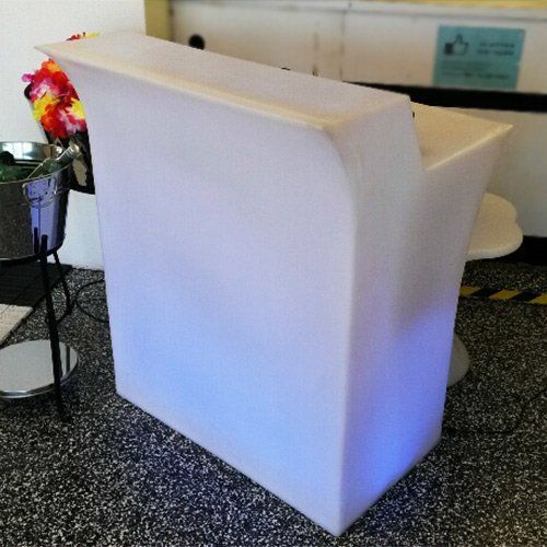 A modern, white, translucent portable bar counter glowing with a blue light at its base in an indoor event setting.