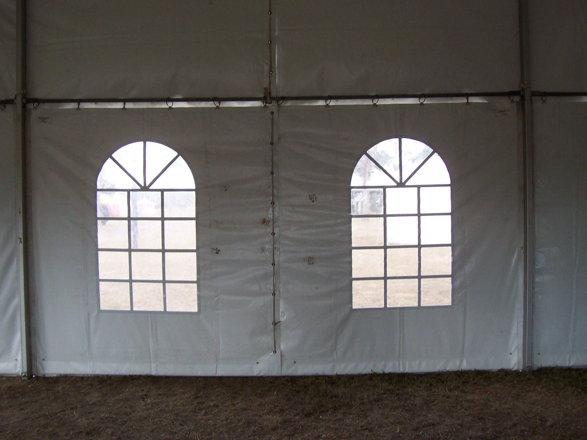 White tent wall with two arched windows with grid frames, looking out onto a grassy area.