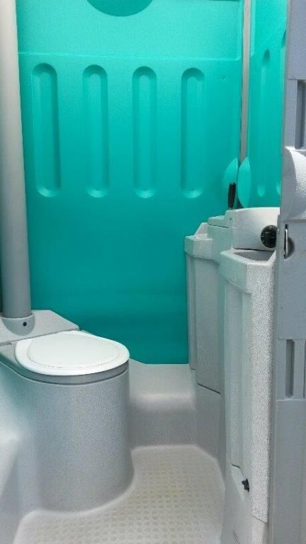 The interior of a teal portable restroom featuring a grey toilet with a white seat and a sink basin attached to the side.
