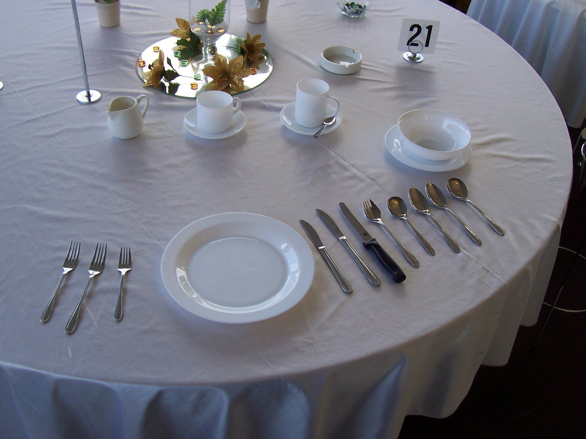 A table setting for a formal meal with a single place setting, including a plate, utensils, and dishes on a white cloth.