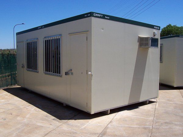 A beige modular portable building with a door, windows with security bars, and an air conditioning unit.