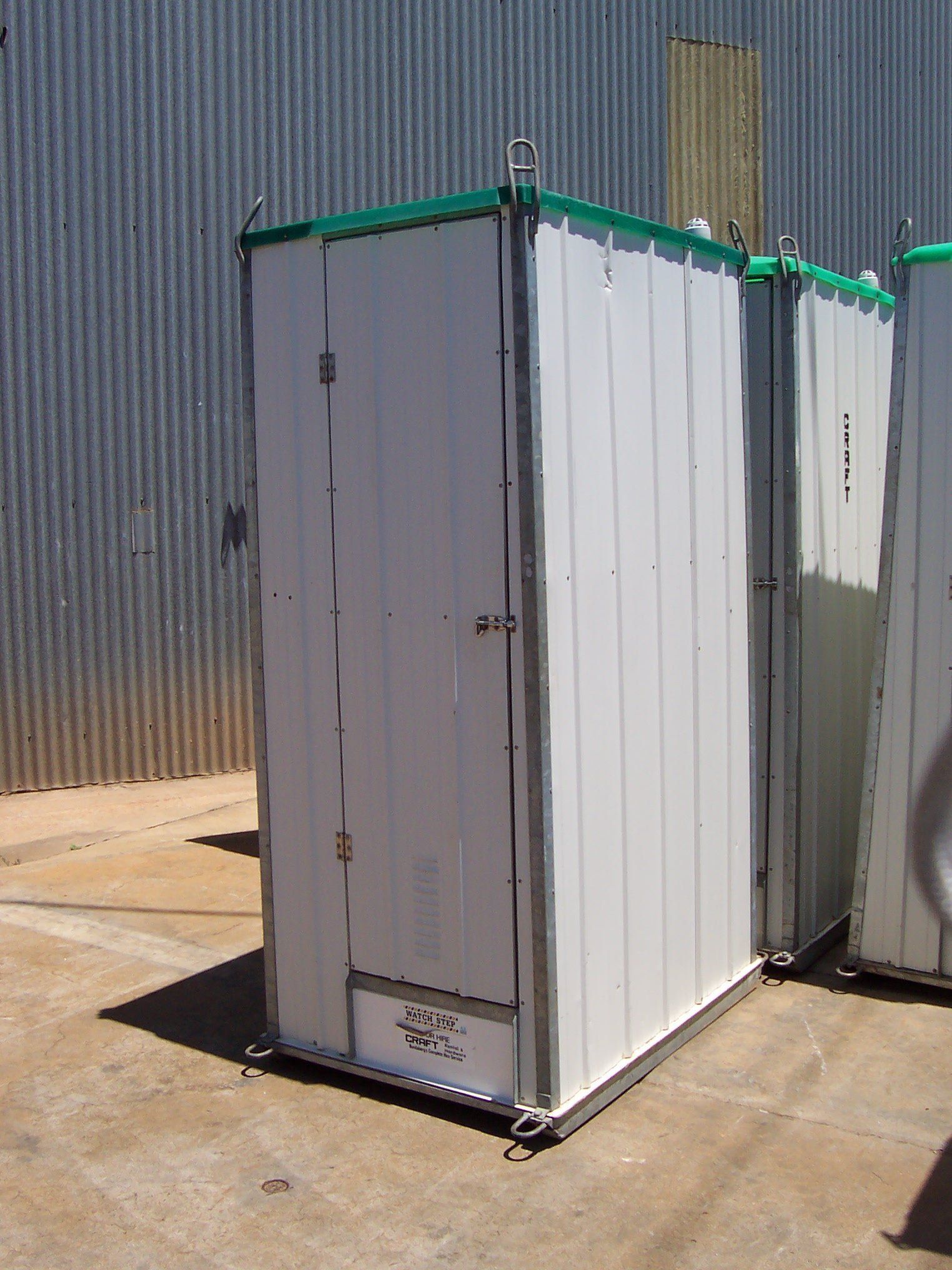 White portable outdoor toilet unit with a green roof trim, standing on a concrete surface.