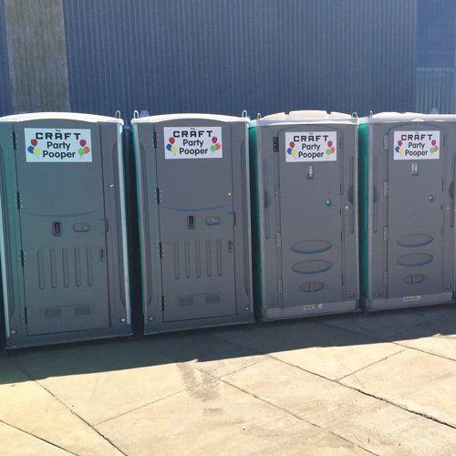 A row of four grey portable toilets sitting on a paved surface, each labeled 