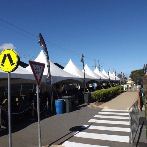 A sidewalk with white pedestrian crossing, a line of white event tents, and a yellow pedestrian crossing sign.
