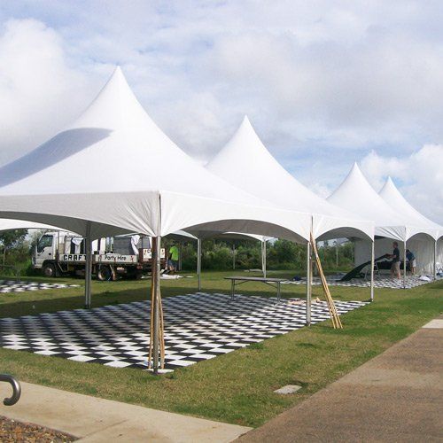 Four white peak tents stand in a row over a black-and-white checkered dance floor on a grassy field.