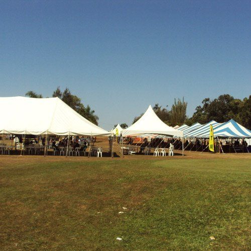 White, blue, and white-striped tents set up on a grassy field under a clear blue sky.