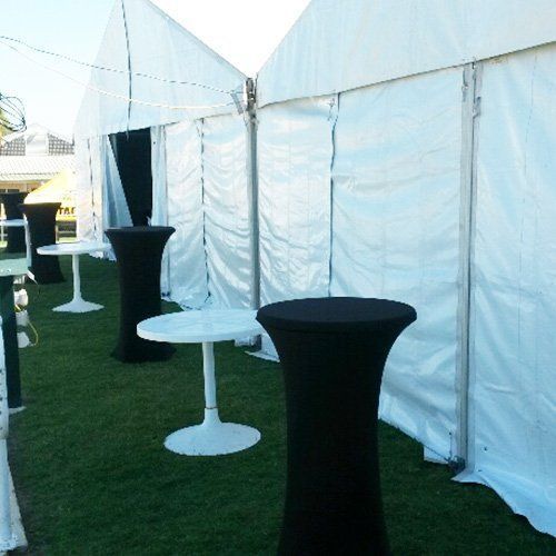 White party tents on a grassy lawn with white low tables and black-covered high-top cocktail tables.