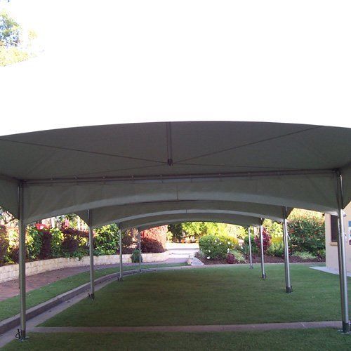A long, beige arched marquee tent set up on a grassy lawn during the day.