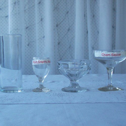 Four varied glassware items lined up on a white cloth surface against a light, sheer curtain background.