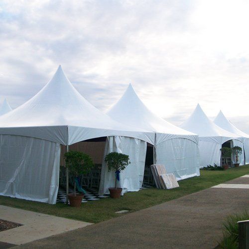 A row of white, pointed-top event tents on a grassy lawn next to a paved pathway.