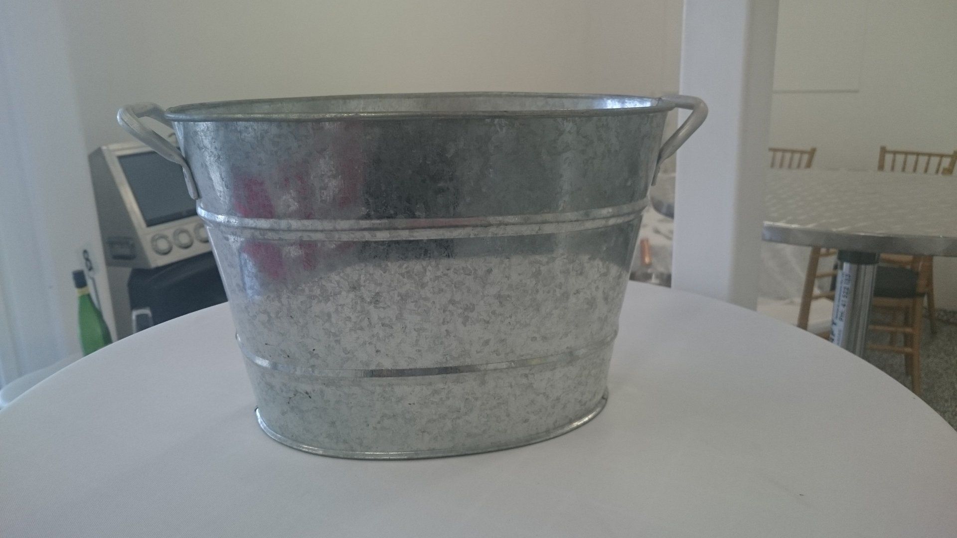 A metal, oval-shaped basin or tub with two side handles sits on a white table.
