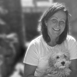 Woman smiling, holding a small, fluffy dog outdoors.