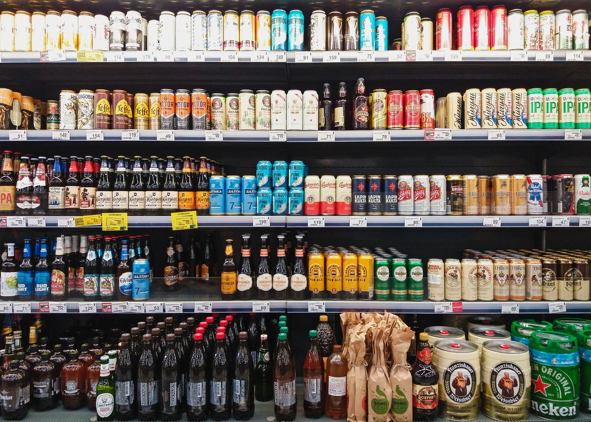 Store shelves lined with assorted bottled and canned drinks in a refrigerated display.