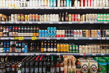 Grocery store beverage aisle with rows of beer, soda, juice, and bottled drinks on shelves