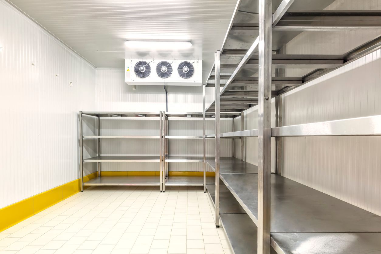 Empty refrigerated storage room with metal shelving and a large ceiling fan unit