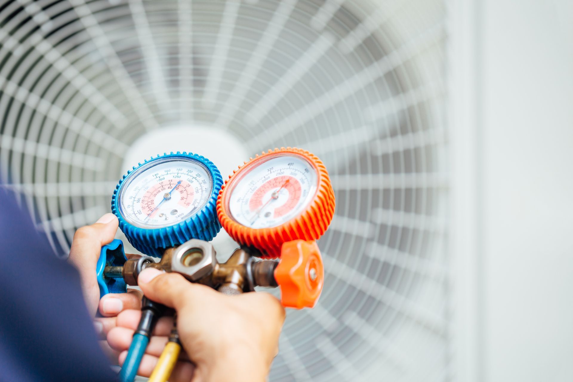 Hands holding blue and orange pressure gauges in front of a fan grille