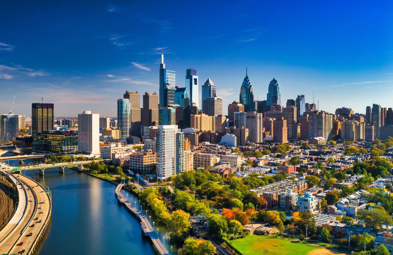 Riverfront city skyline with modern skyscrapers, blue sky, and a curving river in the foreground