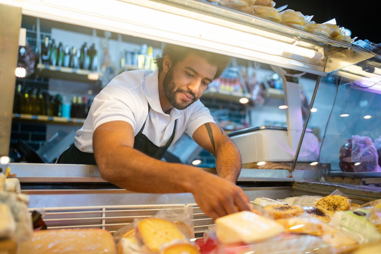 Chef arranging pastries behind a glass counter in a bright bakery, smiling while working