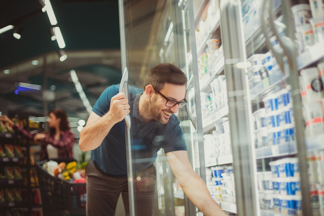 Man cleaning a glass display case in a supermarket aisle using a blue squeegee