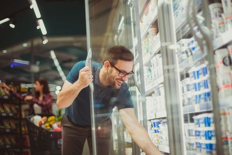 Man cleaning a refrigerated store display with a squeegee, shelves of products behind glass.