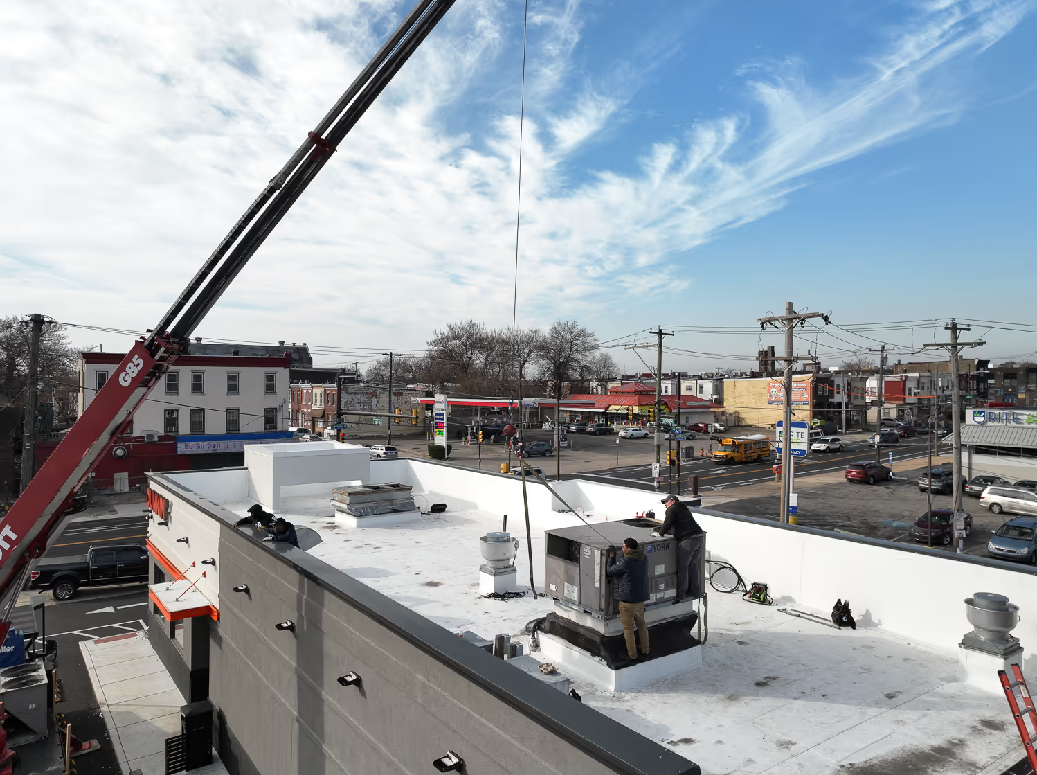 Rooftop worksite with a crane lifting materials over a white industrial building near train tracks