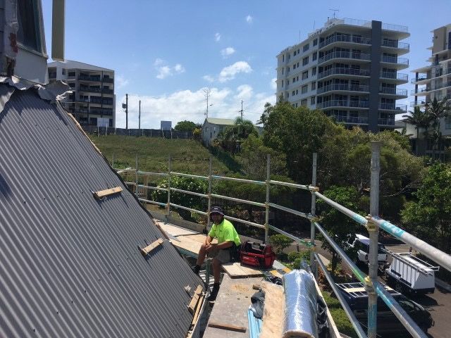 A Man is Sitting on the Roof of a Building — Roofing Revamped in Maroochydore, QLD