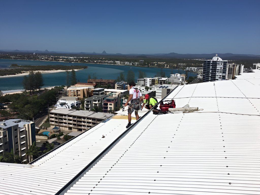 A Man is Standing on Top of a White Roof Overlooking a City — Roofing Revamped in Maroochydore, QLD
