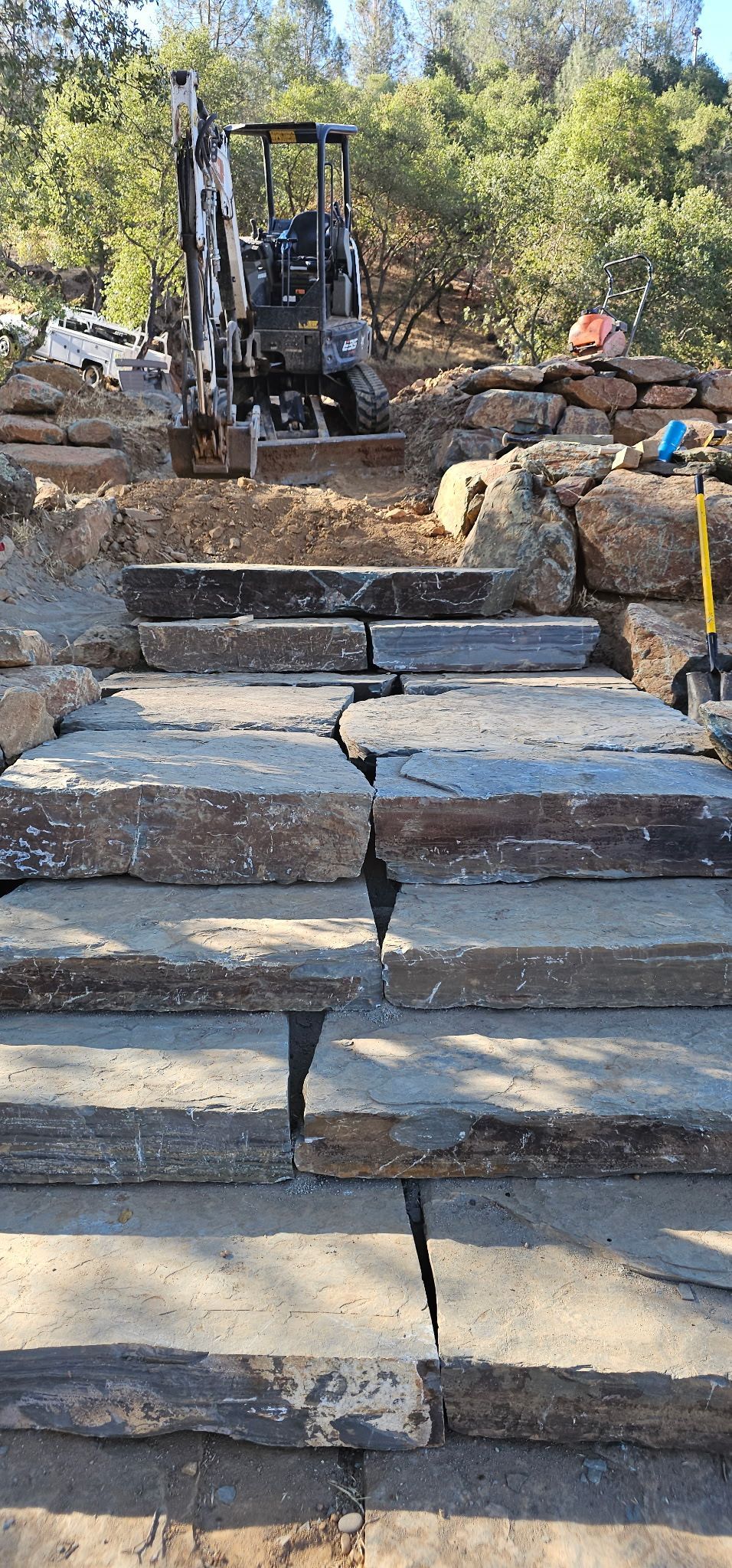 Stone steps leading up a rough, unfinished outdoor path with construction equipment at the top