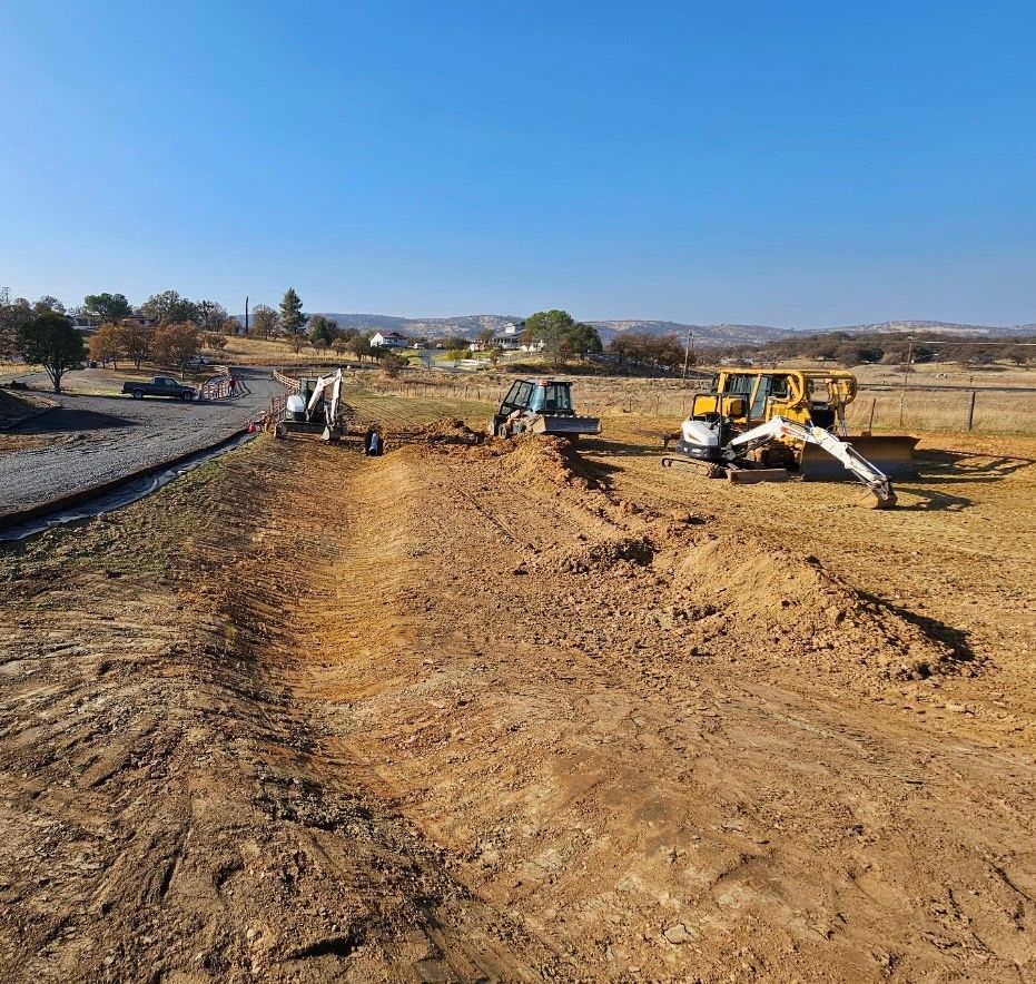 Construction equipment grading a dirt field under a clear blue sky.