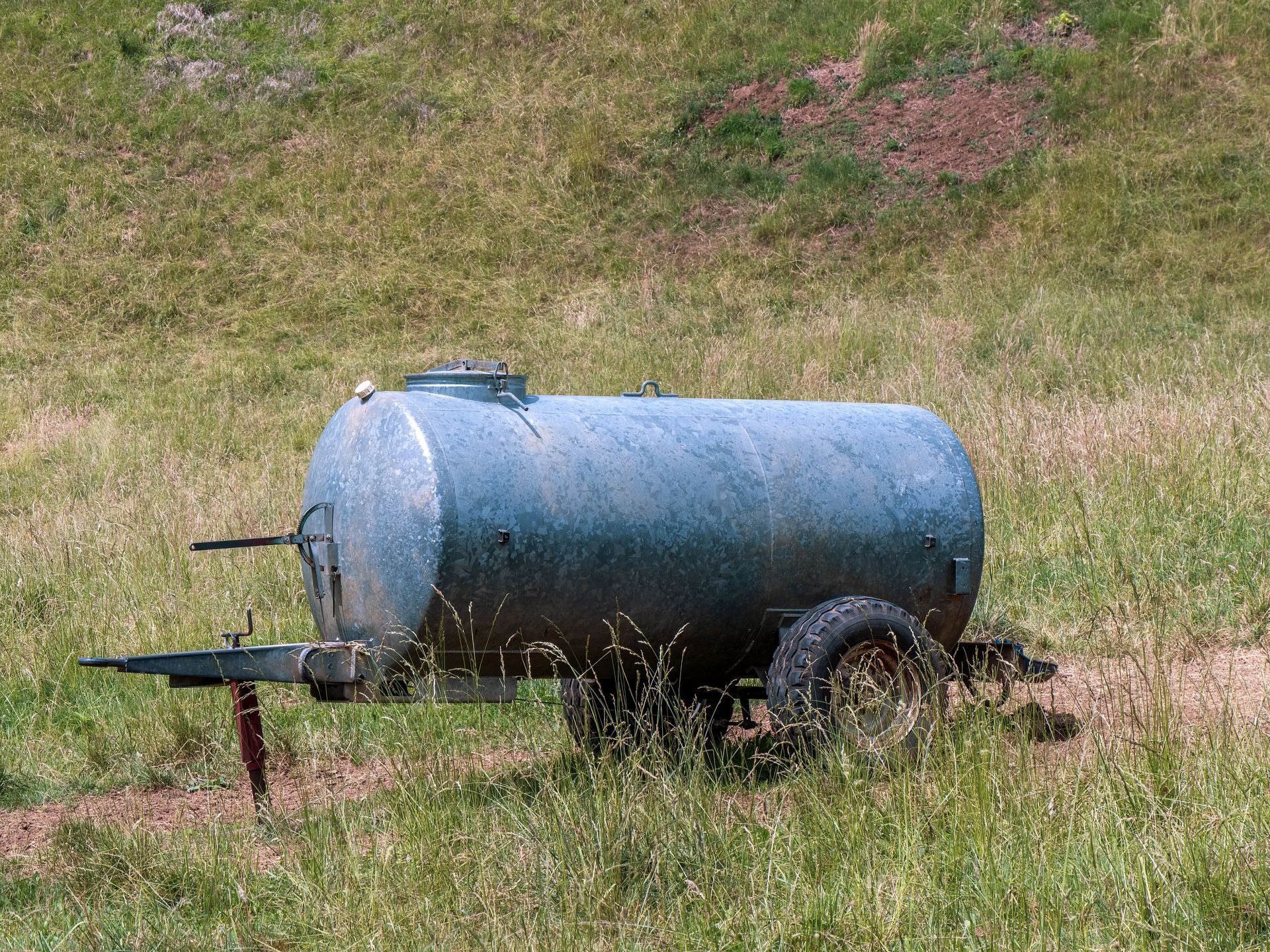 Blue water tank trailer in a grassy field with a small metal stand in front