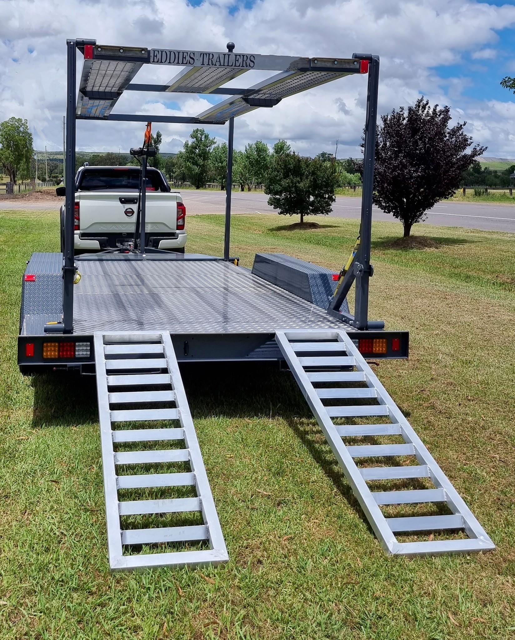 A trailer with ramps attached to it is parked in a grassy field.