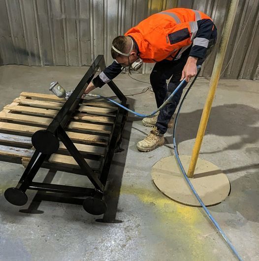 A Man in An Orange Vest Is Spray Painting a Wooden Bench — Eddies Trailers & Fab in Mudgee, NSW