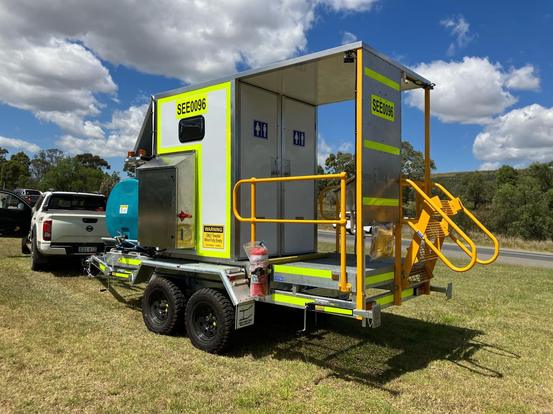 A trailer with stairs attached to it is parked in a grassy field next to a truck.