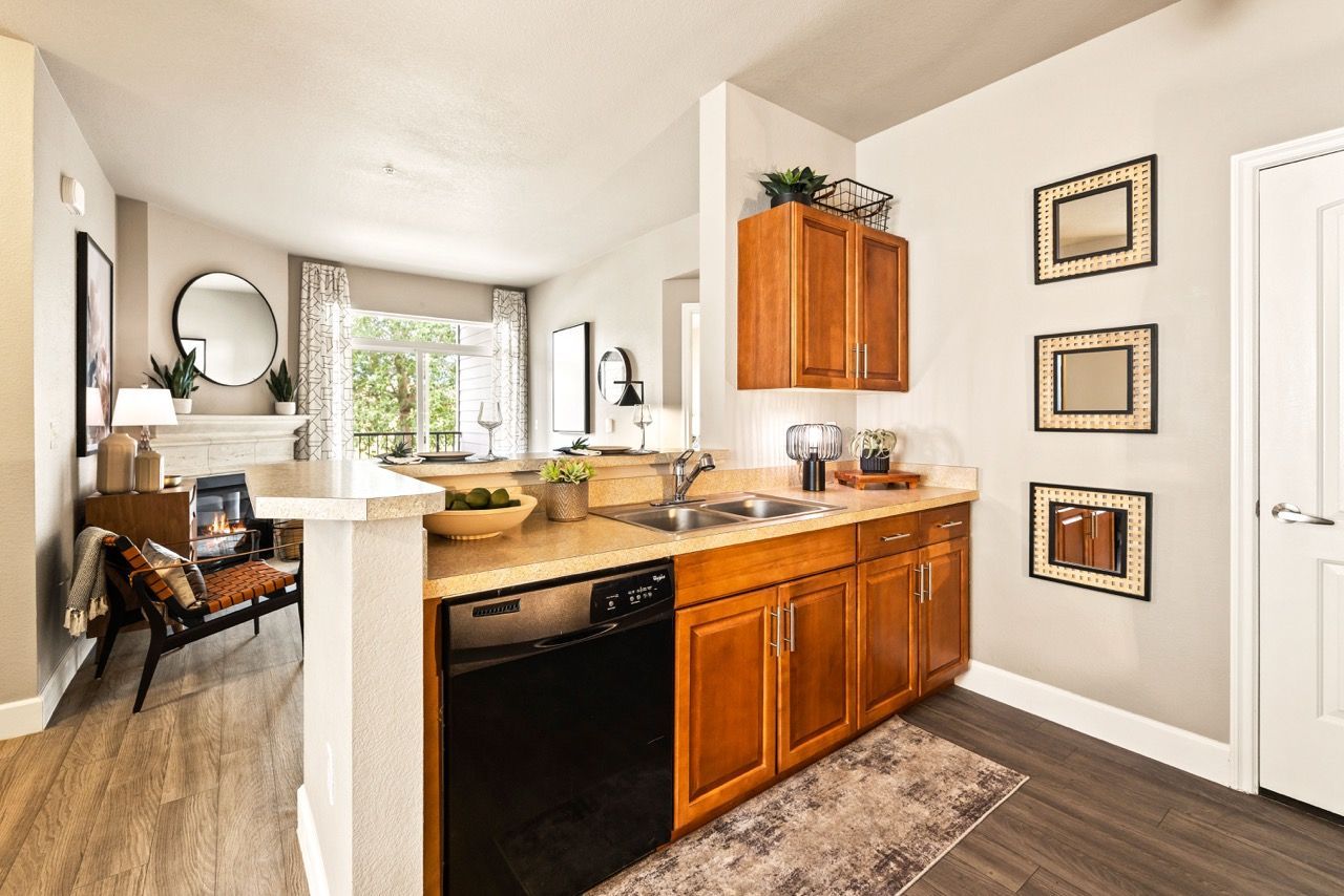 Open-concept kitchen with wood cabinets, double sink, and bar counter; living area visible in back.
