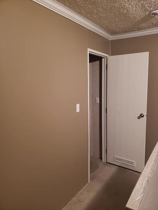 Empty beige hallway with open white door and carpeted floor