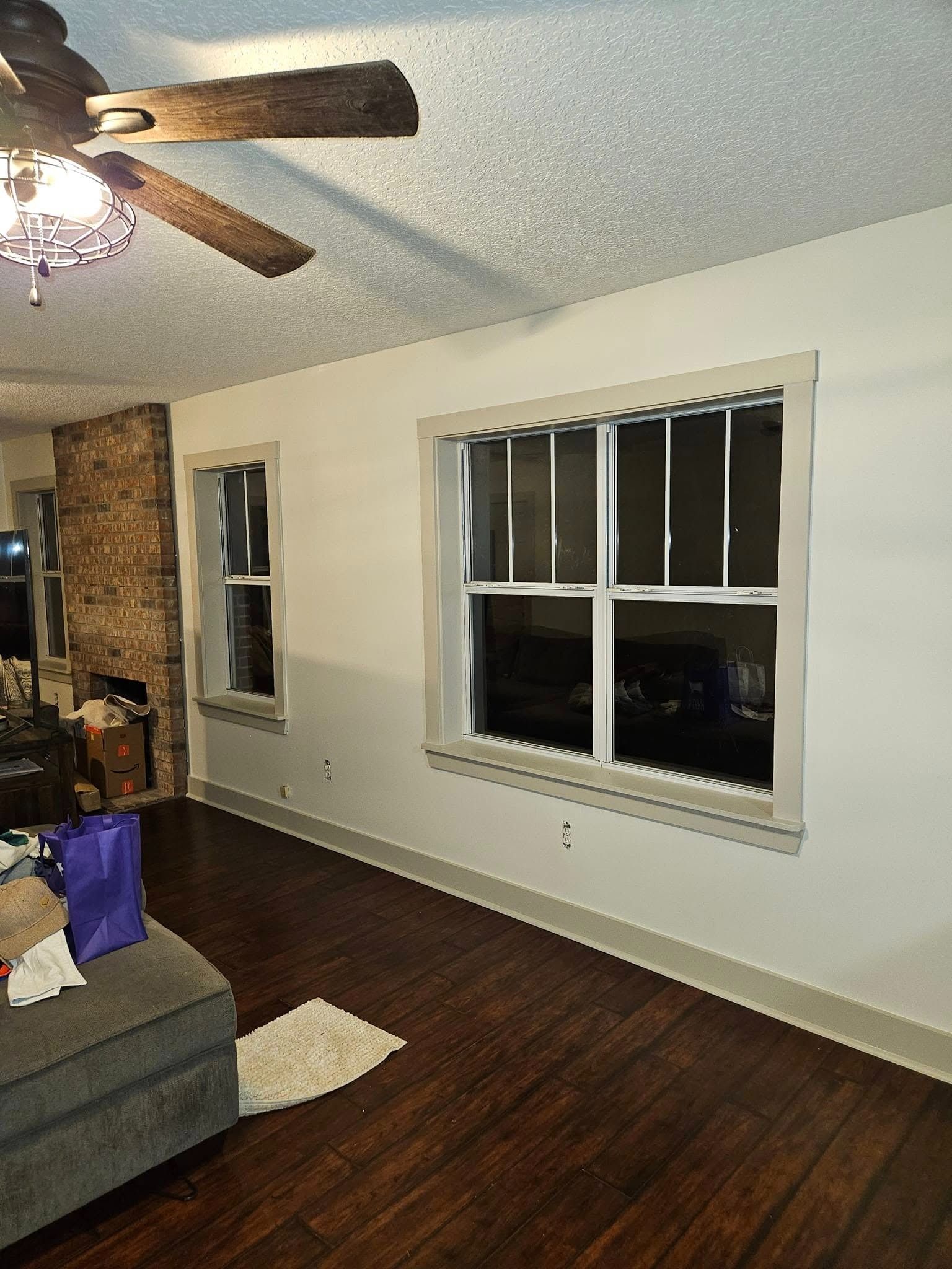 Empty living room with dark wood floors, a ceiling fan, and two windows with blinds at night