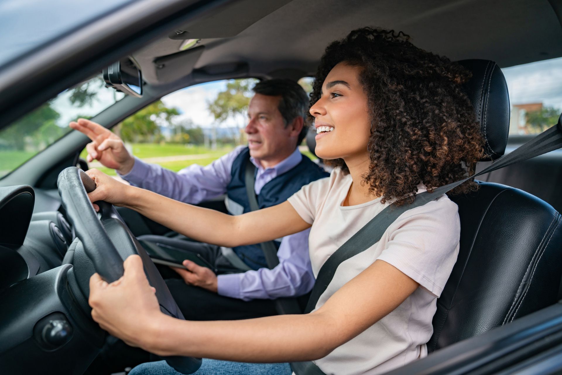 A male professional giving driving instruction to a young woman.