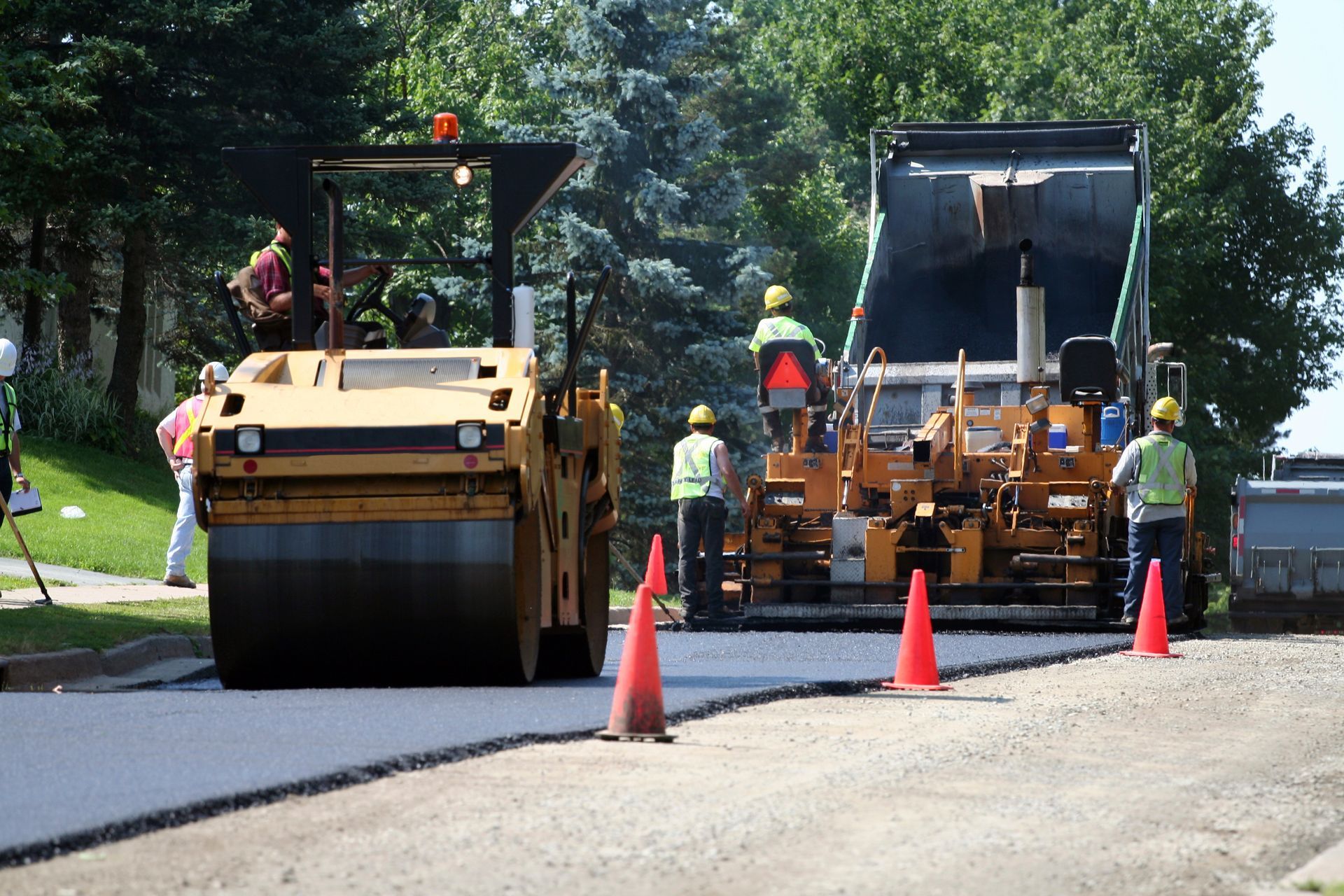 Asphalt contractors are using a spreader to lay the first layer of asphalt on a city street.