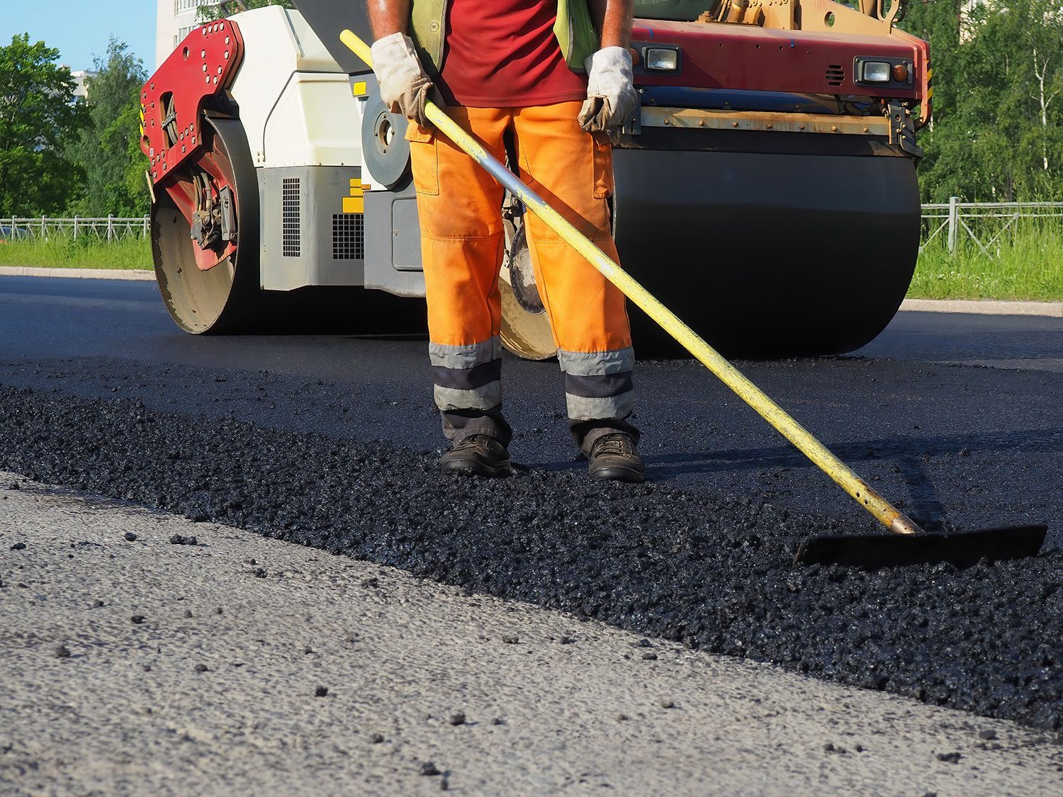 A worker rakes asphalt while a roller smooths for a strong, lasting road finish. A worker rakes asphalt while a roller smooths for a strong, lasting road finish.