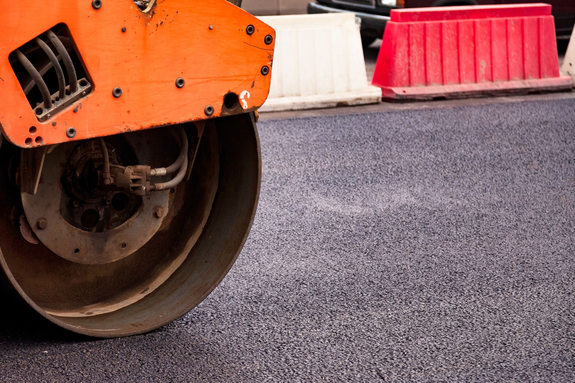 Commercial asphalt contractor operating an orange road roller machine.