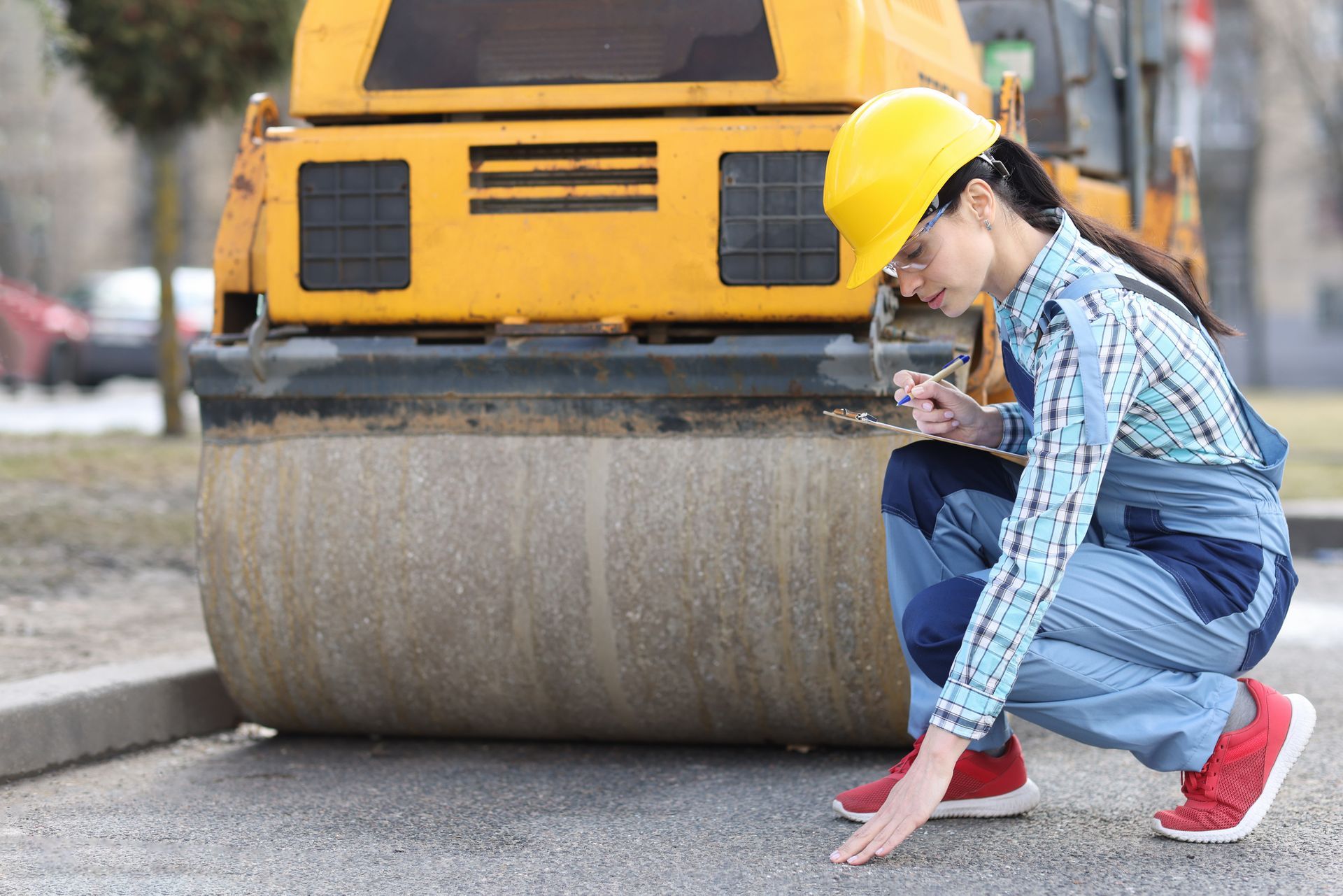 Woman examines asphalt pavement in front of asphalt paver. Woman examines asphalt pavement in front of asphalt paver.