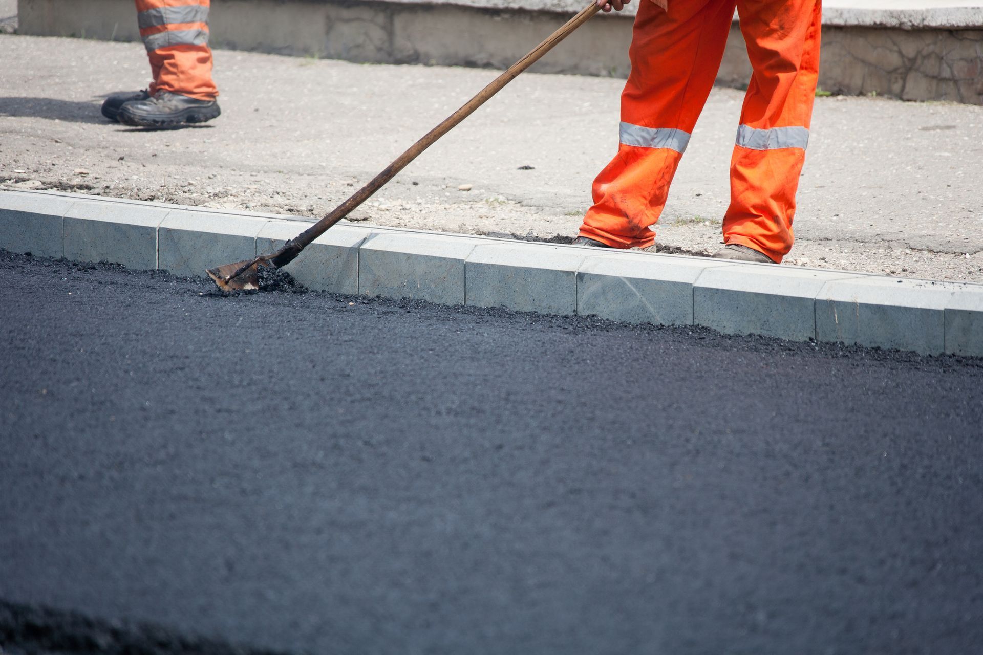 Road worker in orange overalls smoothing asphalt with a rake. Road worker in orange overalls smoothing asphalt with a rake.