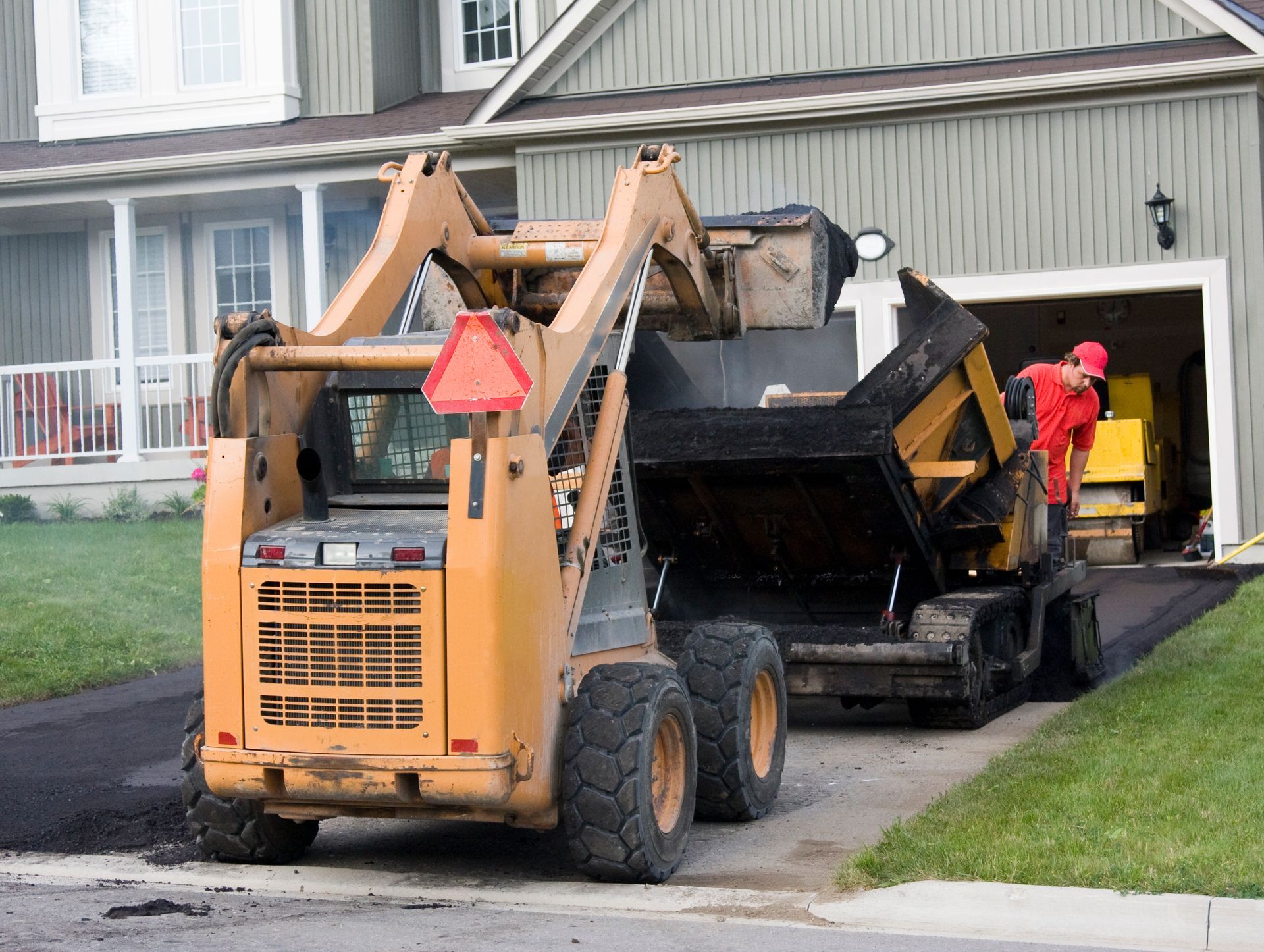 Driveway asphalt contractors operating a paving machine to lay asphalt on a residential driveway.