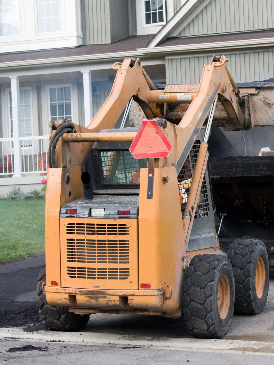 Driveway asphalt contractors operating a paving machine to lay asphalt on a residential driveway.