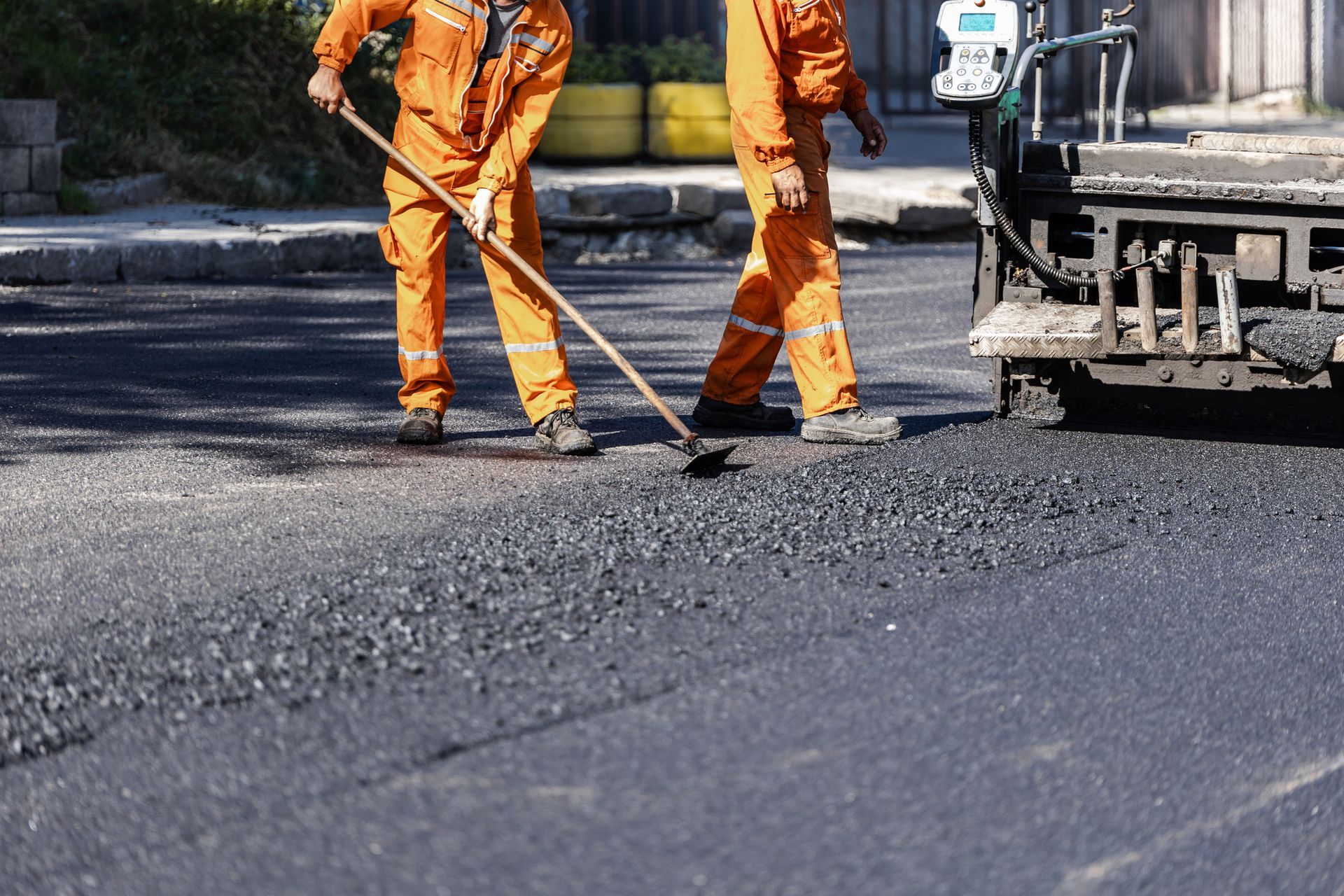 Two workers in orange coveralls paving a road with asphalt, using rakes. Two workers in orange coveralls paving a road with asphalt, using rakes.