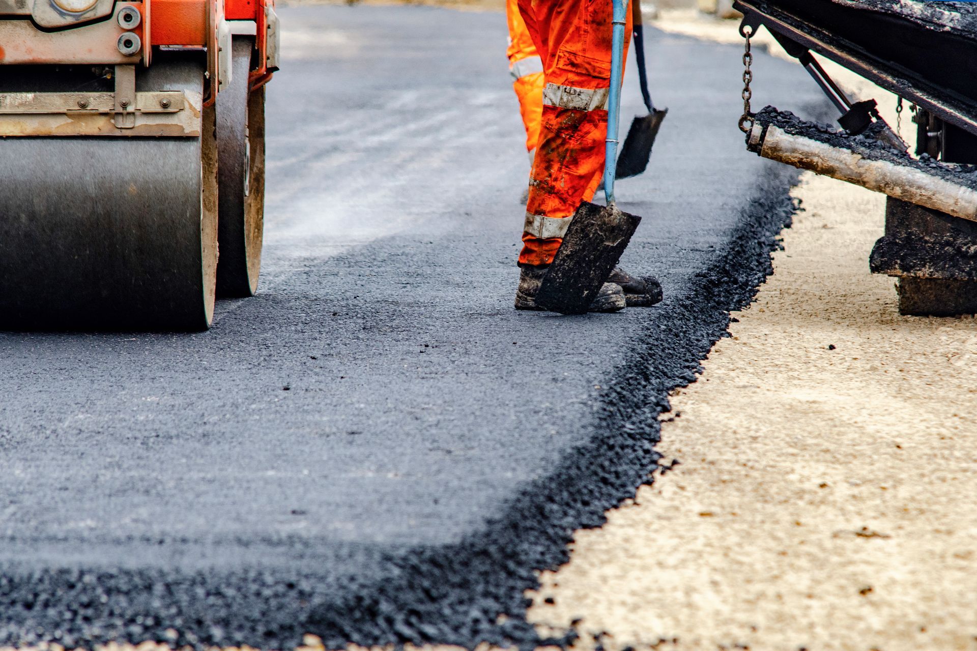 Local paving contractors in high-visibility gear are applying fresh hot asphalt to a road surface.